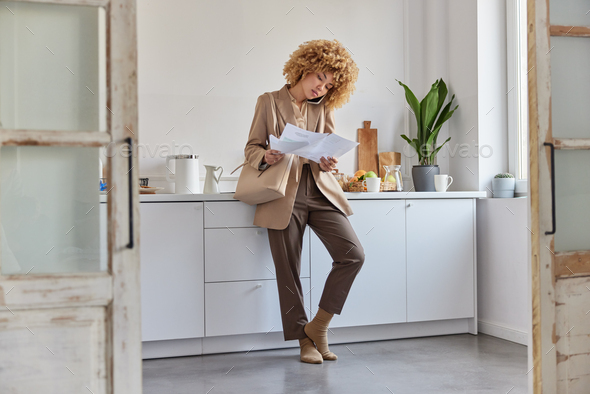 Photo of serious attractive busy female freelancer looks through paper documents makes phone call - Stock Photo - Images