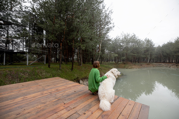 Woman with dog on pier near lake in pine forest - Stock Photo - Images