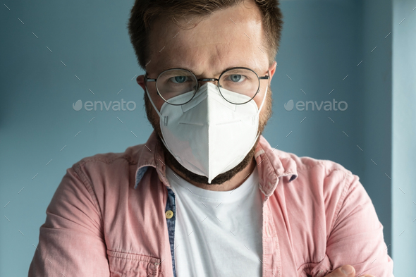 Close-up of a serious man in glasses and a medical mask, stands on a blue background. Health concept - Stock Photo - Images