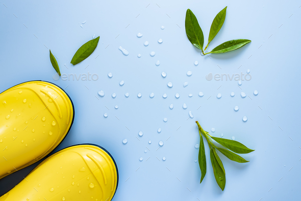 Yellow rubber boots stand next to a snowflake made of water drops and scattered green leaves - Stock Photo - Images
