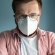 Close-up of a serious man in glasses and a medical mask, stands on a blue background. Health concept - PhotoDune Item for Sale