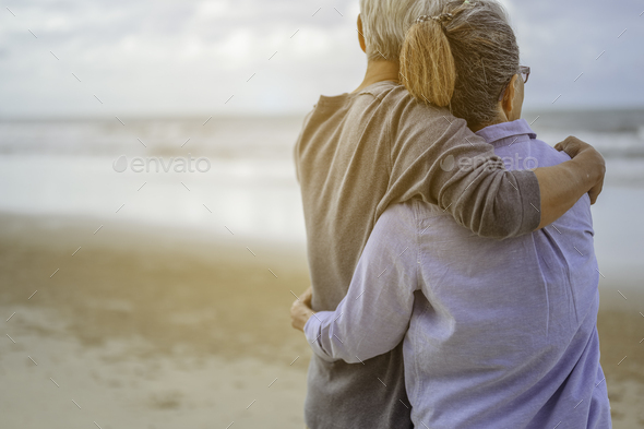 A senior couples embrace the beach in the morning, look at the bright blue skies