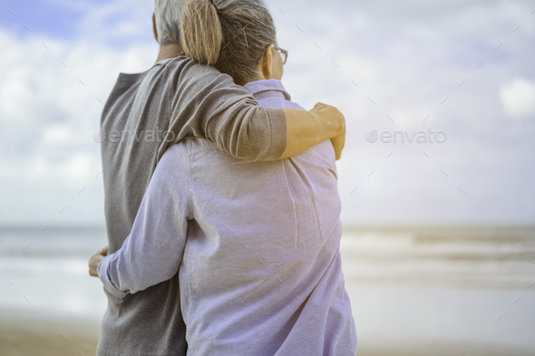 A senior couples embrace the beach in the morning, look at the bright blue skies and plan life