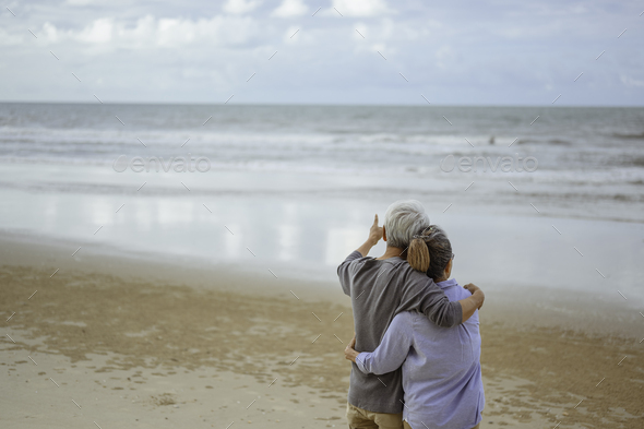 A senior couple hugged each other at the beach in the morning. The old man pointed the finger