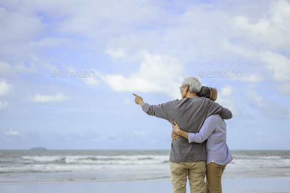 A senior couple hugged each other at the beach in the morning. The old man pointed the finger