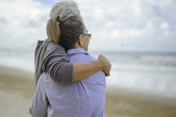 A senior couples embrace the beach in the morning, look at the bright blue skies and plan life