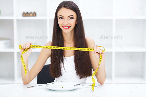 Diet. Happy young smiling woman about to eat one pea holding plate and fork with tape measure.