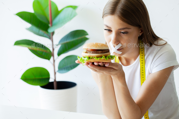 Young woman with duct tape over her mouth, preventing her to eat junk food.