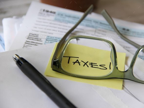 The word Taxes through the glasses of a person filing taxes with tax forms in background  - Stock Photo - Images