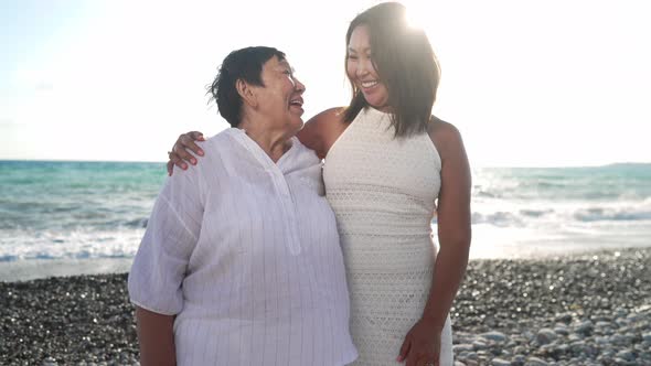 Happy Asian Daughter and Old Mother Talking Standing at Sunset on Picturesque Mediterranean Sea alt