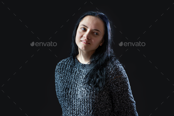 portrait of young woman with long dark hair wearing gray knitted sweater over black background - Stock Photo - Images