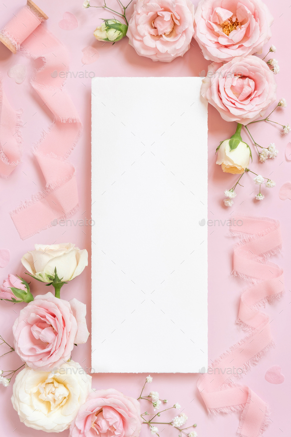 Blank paper card between pink roses and pink silk ribbons on pink top view, wedding mockup - Stock Photo - Images