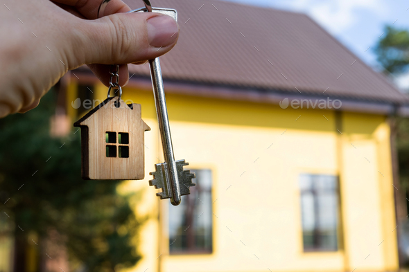 A hand with the keys to a new house on the background of an unfinished cottage.