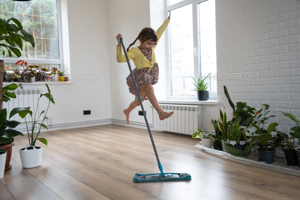 A girl dances with a mop to clean the floor in a new house - general cleaning in an empty room