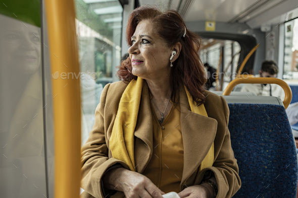 mature woman listens to music with headphones while traveling in public transport on the way to work - Stock Photo - Images