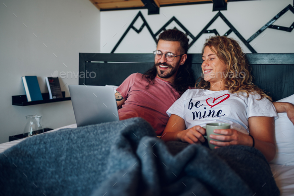 Romantic couple lying in the bed at home in the morning and using laptop - Stock Photo - Images