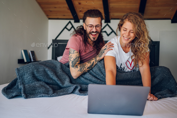 Romantic couple lying in the bed at home in the morning and using laptop - Stock Photo - Images