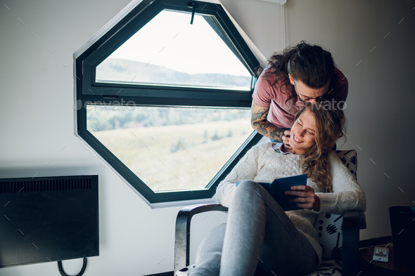 Man is embracing his girlfriend while she is reading a book at home - Stock Photo - Images