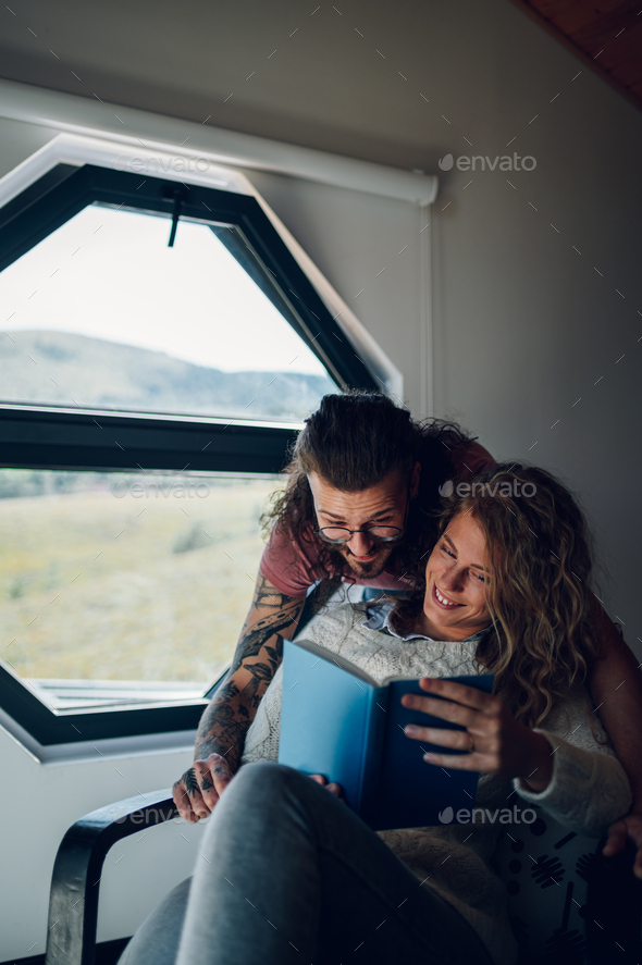 Man is embracing his girlfriend while she is reading a book at home - Stock Photo - Images