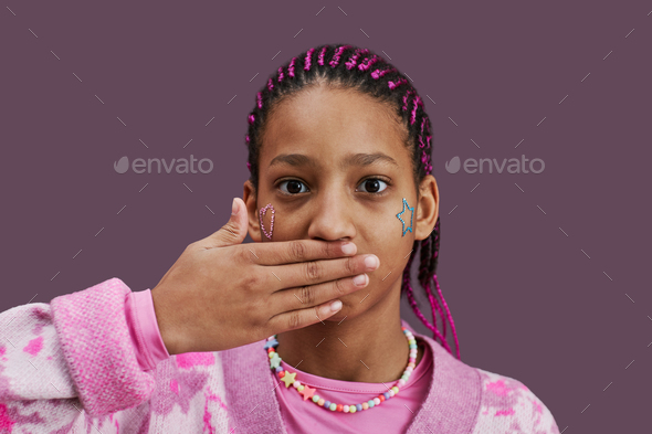 Black teenage girl closing mouth at camera against pink background - Stock Photo - Images