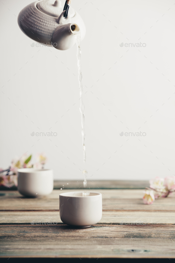 Pouring hot tea into porcelain cup on wooden table background - Stock Photo - Images