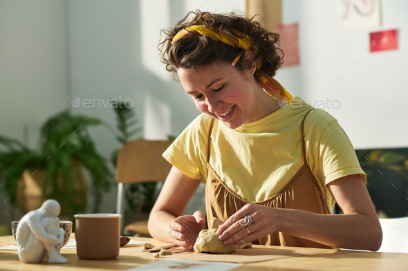 Happy young creative woman in casualwear creating clay human face - Stock Photo - Images