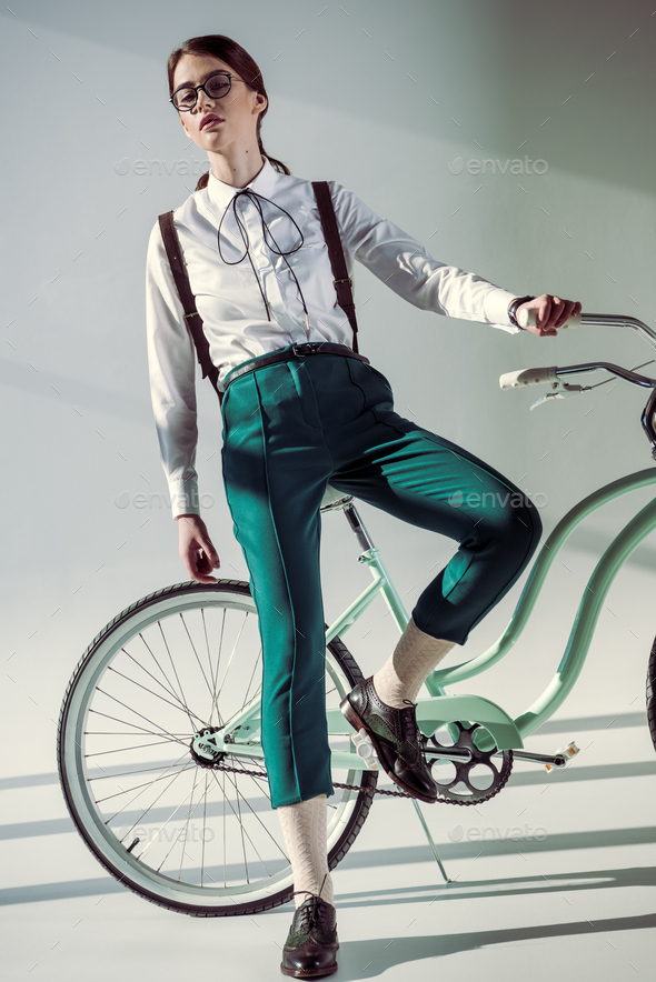 stylish hipster woman in glasses, white shirt and green trousers with hipster bicycle