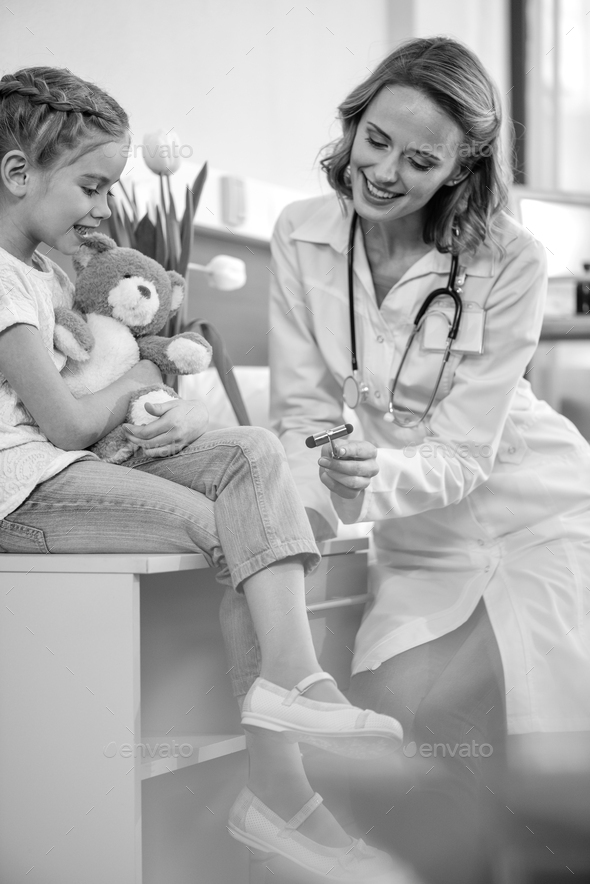 side view of smiling doctor examining girl with reflex hammer, black and white photo