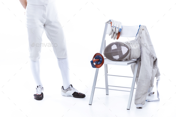 Low section of young man professional fencer standing near chair with fencing equipment isolated on