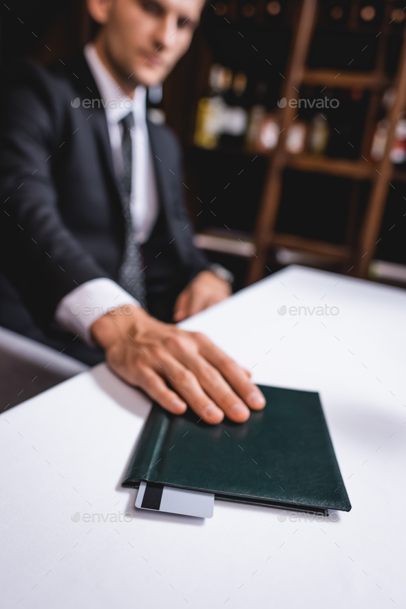 Selective focus of man in suit putting restaurant bill with credit card on table