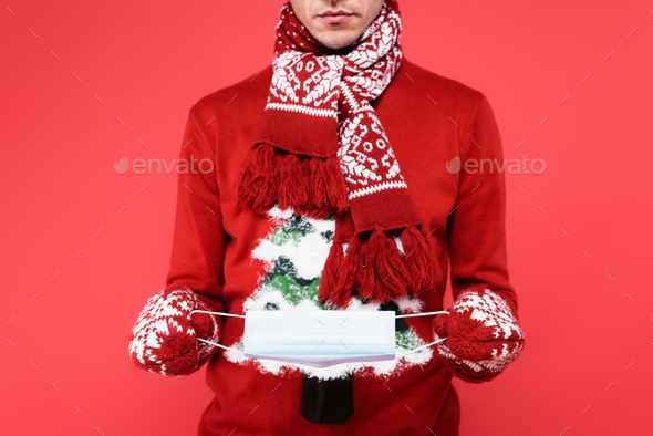 Cropped view of man in scarf and mittens holding medical mask isolated on red