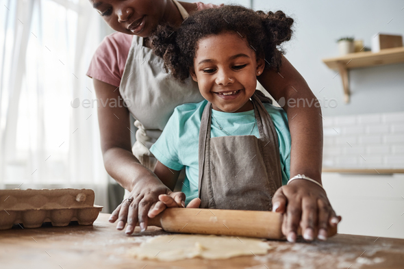 Loving mother and daughter baking together at home and rolling dough - Stock Photo - Images