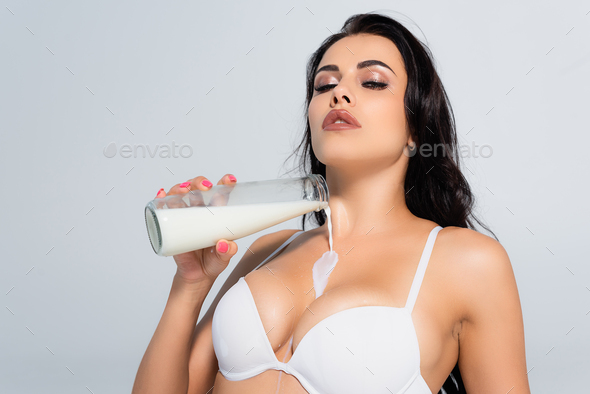 brunette woman in bra holding bottle and pouring milk on bust