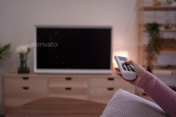 Young Asian woman sitting indoor at home watch tv holding remote control on sofa.