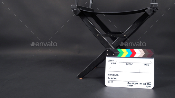 Clapperboard or movie slate with director chair on black background.
