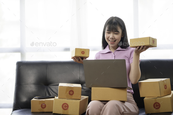 Beautiful Asian online business owner prepares parcel boxes for customer. Check balance and correct