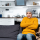 shivering man in knitted sweater and hat sitting on sofa with crossed arms in cold kitchen - PhotoDune Item for Sale