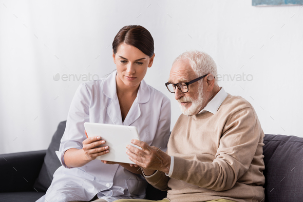 brunette geriatric nurse and elderly man using digital tablet together - Stock Photo - Images