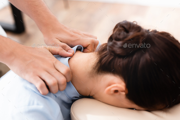 Close up view of masseur doing seated massage of neck for brunette woman on blurred background
