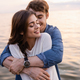 Young man hugging brunette girlfriend with closed eyes beside sea at sunset - PhotoDune Item for Sale