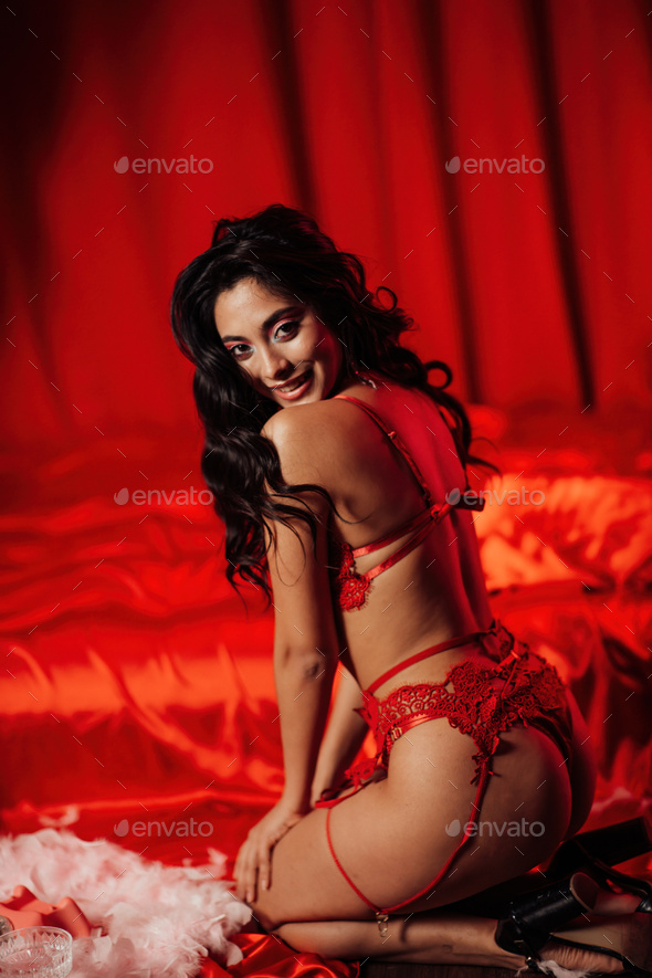 Portrait of smile sexy asian girl glam makeup in red lingerie sits near bed at valentines day decor - Stock Photo - Images