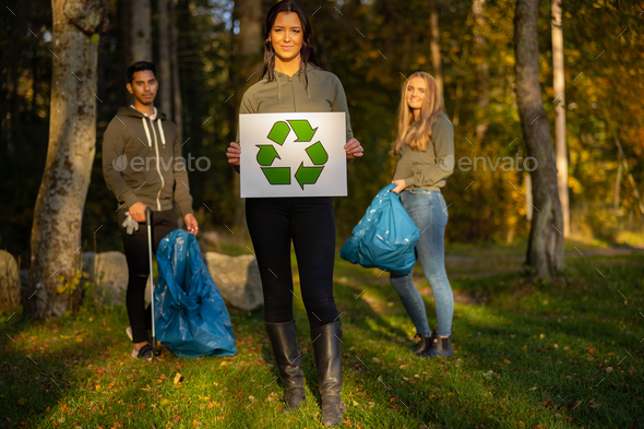 Confident volunteer woman holding recycling symbol placard in front of team - Stock Photo - Images