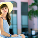 Young woman wearing light summer dress and yellow straw hat sitting outside near hotel - PhotoDune Item for Sale