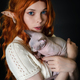 Portrait of young woman cosplayer elf in white knitted dress hugging Sphinx kitten. Black background - PhotoDune Item for Sale