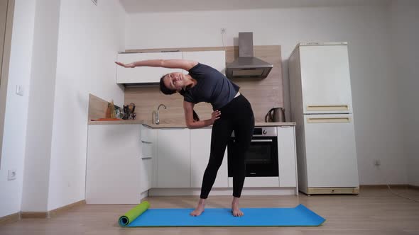 Energetic Brunette Girl Does Exercise on the Gym Mat at Home in the Kitchen