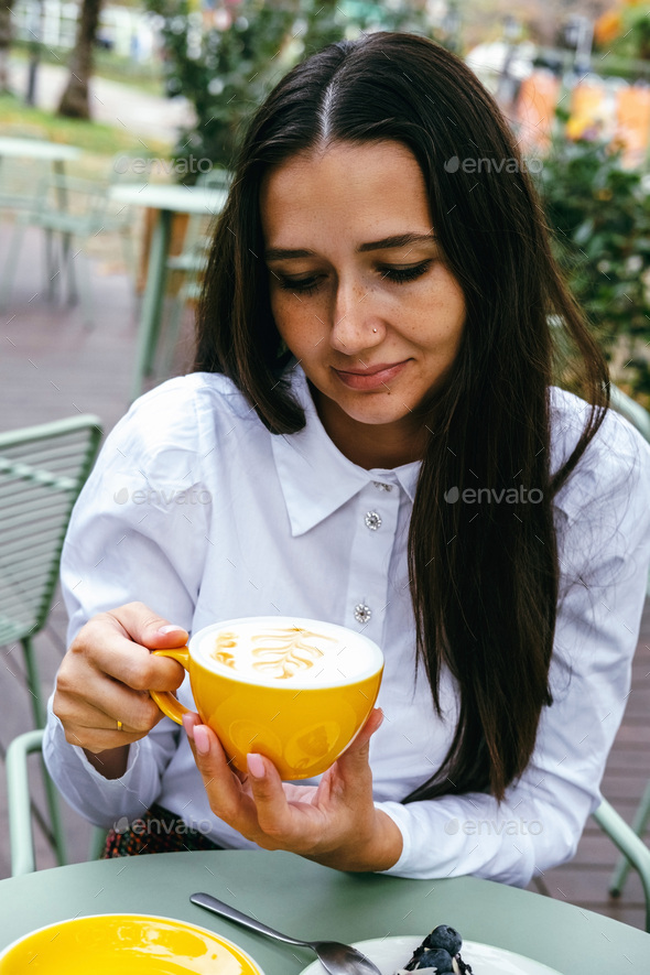 Pretty young brunette woman holding yellow coffee cup in restaurant.  - Stock Photo - Images