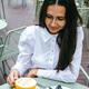 Happy brunette woman drinking coffee and eating blueberry cheesecake at outdoor cafe.  - PhotoDune Item for Sale