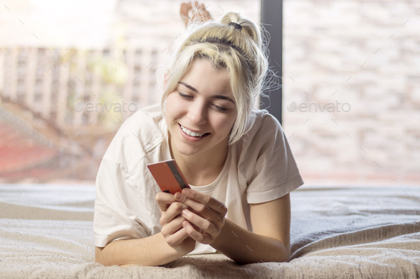 young woman relaxing on bed at home, holding credit card, shopping. - Stock Photo - Images