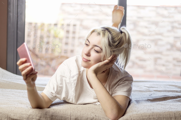 Relaxed woman using a smart phone in the morning on the bed at home - Stock Photo - Images