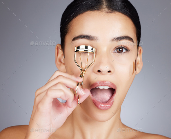 Wow, face and woman with eyelash curler in studio isolated on a gray background. Portrait, makeup s